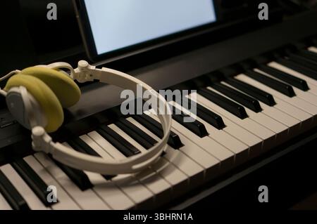 White headphones placed on electric piano keys and a blank tablet screen. Stock Photo