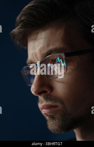 Close up of businessman analyzing trading data late at night, staring at a monitor with stock indexes and economic charts reflecting in his glasses, evaluating investment strategies on crypto market. Stock Photo