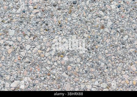 A full-frame close-up shows a light gray concrete surface embedded with small rocks of various colors and shapes. Stock Photo