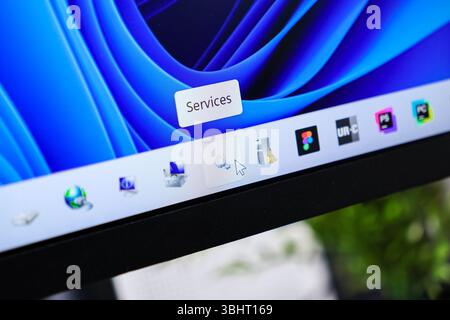 Poznan, Poland - June 6, 2025: Close-up of a mouse cursor hovering over an application icon on a taskbar, revealing a 'Services' tooltip, showing syst Stock Photo