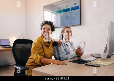 Female colleagues shar a friendly moment in a modern office environment, highlighting cooperation and positive workflow during project management acti Stock Photo