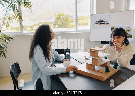 Two women engage in a creative planning session, discussing an architecture project with enthusiasm and focus. Stock Photo