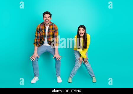 Happy young couple posing enthusiastically in casual vibrant clothing against a turquoise background capturing fun moments Stock Photo