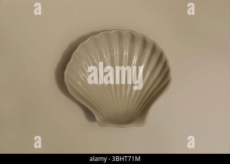 Ceramic plate seashell shaped on beige table background. Neutral tones, soft lighting, empty copy space. Summer sea coastal, minimalistic aesthetic Stock Photo