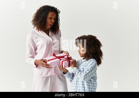 Happy Black daughter gives pink gifts to joyful mom in PJs. Stock Photo