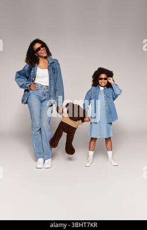 Black mom and daughter in denim, grey studio. Stock Photo