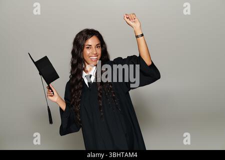 Young woman in a graduation gown joyfully celebrating her academic achievement with a hat Stock Photo