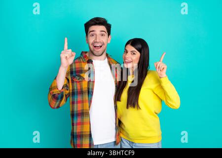 Cheerful young couple pointing up on a turquoise background, happiness and positive communication concept Stock Photo