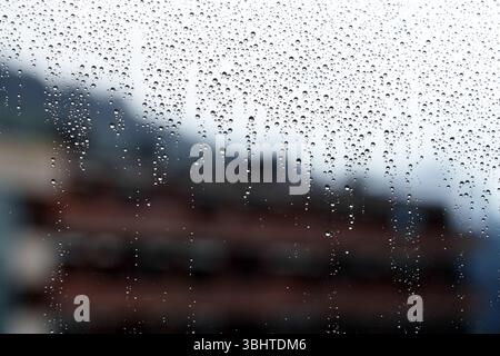 Window covered with rain drops against the background of city building. Close up Stock Photo