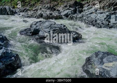 A close-up view of bright teal river rapids rushing over jagged grey rocks, capturing the powerful flow and textured details of this natural freshwate Stock Photo