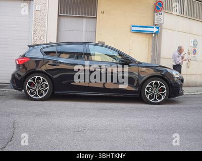 Cremona, Italy - June 2nd 2025 Shadow Black Ford Focus ST Line X fourth generation five door hatchback parked near a wall with an elderly man using a Stock Photo