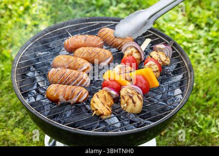 freshly grilled sausages and chicken vegetable skewers on charcoal grill in the garden Stock Photo