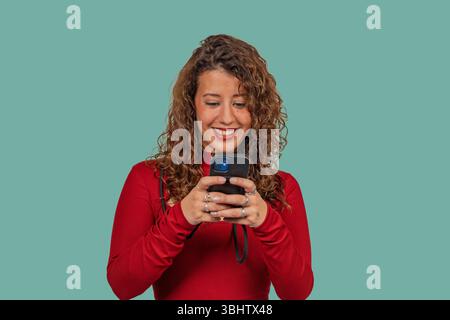 Studio shot of a cheerful young woman using a smartphone against a turquoise background Stock Photo
