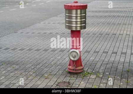 Borken, NRW, Germany, Red fire hydrant with silver cap standing on grey cobblestone street near asphalt road, Europe Stock Photo