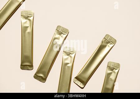 Multiple Golden Foil Stick Packs and Sachets on Beige Background. Mockup for a Quick Food Product, Skincare or Medicine. Stock Photo