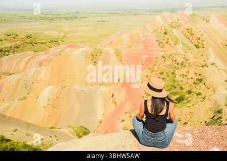 Woman tourist enjoy nature sit relax on colorful vibrant striped hills Mravaltskaro rainbow mountains, Georgia, with unique layered terrain expansive Stock Photo