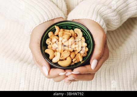 Cashew nuts in green bowl. Hands gently offering healthy snack. Vegan protein food. High energy nutrition. Close up flat lay. Clean eating concept. Stock Photo