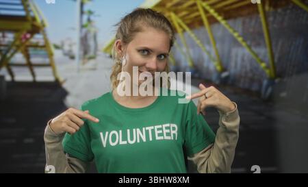 Woman wearing a shirt is pointing in a studio at volunteer blonde young wearing a tshirt and green earring. Stock Photo