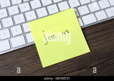 Paper note with phrase Join Us and keyboard on wooden table, closeup Stock Photo