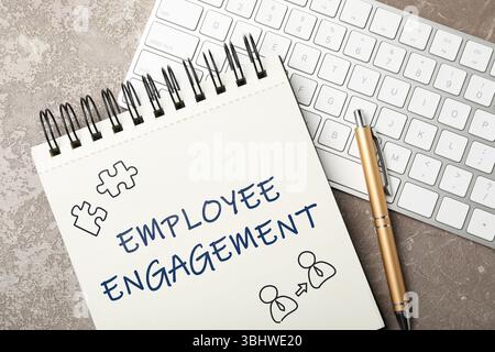 Employee engagement. Words and drawings in notebook, pen and computer keyboard on grey table, top view Stock Photo