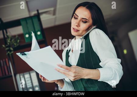 Confident businesswoman multitasking at work, reviewing documents while on a phone call in an office environment Stock Photo