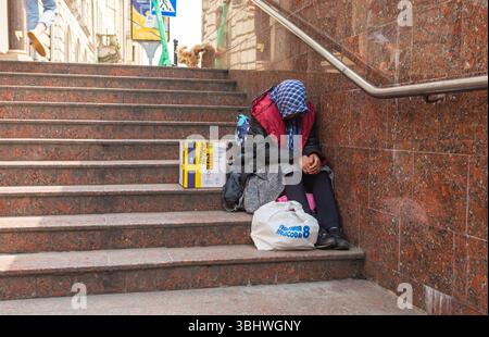 Lviv, Ukraine - Jun. 01, 2025: A person sits on the steps of a building with a bag and box. Stock Photo