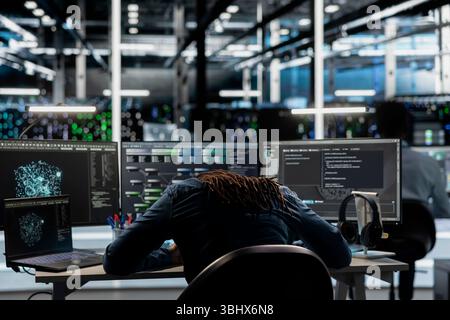 Exhausted server farm engineer falls asleep while using AI algorithms to analyze large datasets. Tired data center worker exhausted after using deep learning to recognize patterns in facility data Stock Photo