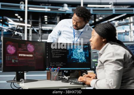 IT staff members in artificial intelligence server hub facility trying to protect servers from hackers. AI data center cybersecurity division colleagues protecting rigs during security breach Stock Photo