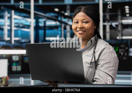 Portrait of smiling data center software developer using artificial intelligence neural networks. Cheerful server farm worker uses AI programming language on computer, configuring specialized hardware Stock Photo
