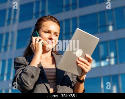 Professional woman using digital tablet during phone call outdoors in city Stock Photo