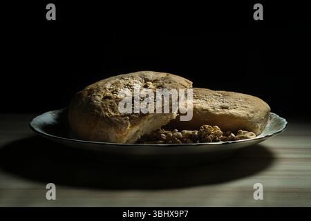 Two loaves of homemade bread with sesame seeds are placed on a plate with walnuts, creating a rustic, wholesome image Stock Photo