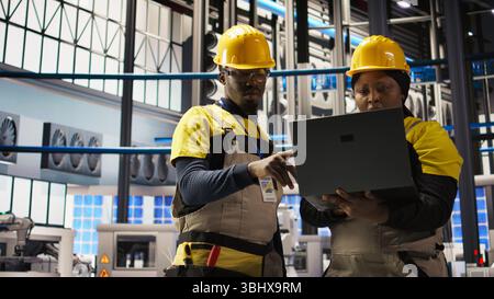 Engineering team doing brainstorming in smart factory, analyzing IoT sensor data. Industry 4.0 plant teamworking colleagues managing operational reliability of photovoltaic systems, camera A Stock Photo