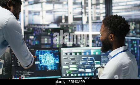 Pleased data center manager praising work done by engineer using neural network models to configure hardware. Supervisor congratulating employee for successfully using AI to optimize system, camera B Stock Photo