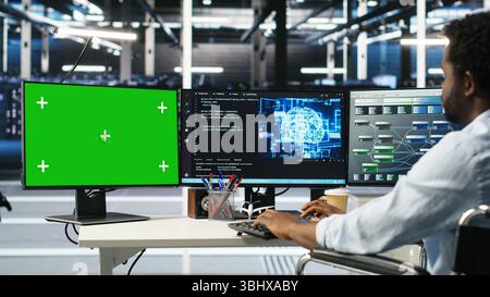 Data center engineer with paraplegia using AI deep learning algorithms on green screen PC to analyze datasets. Server room worker in wheelchair at chroma key PC using AI neural networks, camera B Stock Photo