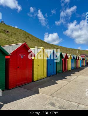 Colourful beach huts against hillside, on the coast at Whitby, Yorkshire, England Stock Photo