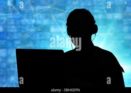 A military cyber security specialist in the digital battlefield. The silhouette of a serviceman with a headset behind a laptop is a concept of informa Stock Photo