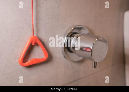 Red Emergency Pull Cord with Metal Fixture on Bathroom Wall Stock Photo