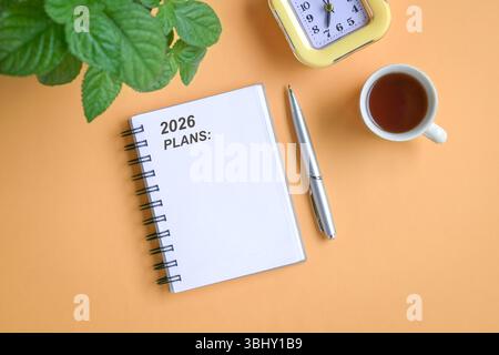 2026 plans on notepad, next to cup of coffee, clock, pen and green plant. Top view. Stock Photo