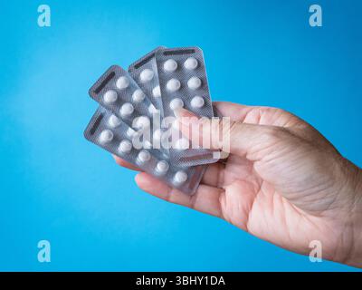 Woman holding several strips of pills or medication. Isolated on blue background. Stock Photo