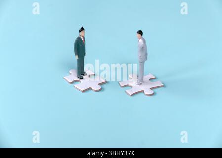 Two Businessmen Standing on Separate Jigsaw Puzzle Pieces: Highlighting Communication and Coordination Challenges Stock Photo