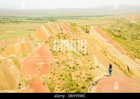 Woman tourist enjoy nature walk on colorful vibrant striped hills of Mravaltskaro rainbow mountains, Georgia, with unique layered terrain expansive st Stock Photo