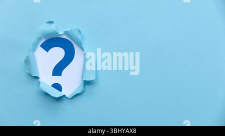 Torn Paper Revealing Blue Question Mark on Light Blue Background Stock Photo