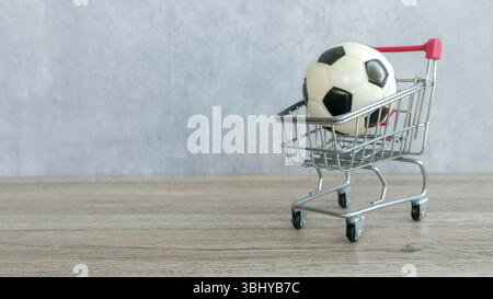 Soccer Ball in Mini Shopping Cart on Wooden Surface with Gray Background Stock Photo
