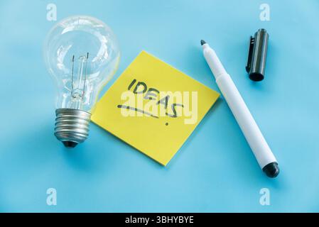 Creative Ideas Concept with Light Bulb, Sticky Note, and Pen on Blue Background Stock Photo