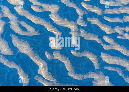 Troughs in the sand caused by receding seawater create deep shadows. Stock Photo