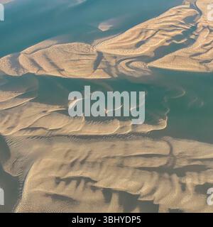 The wind and sea have created ripple textures on the exposed sand. Stock Photo
