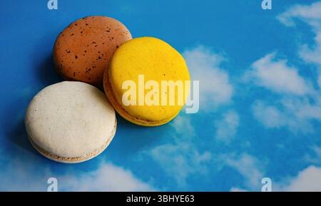Fancy color assorted macarons in blue sky background, French snack, pastry recipe, almond flour, macaroons biscuits dessert with copy space Stock Photo