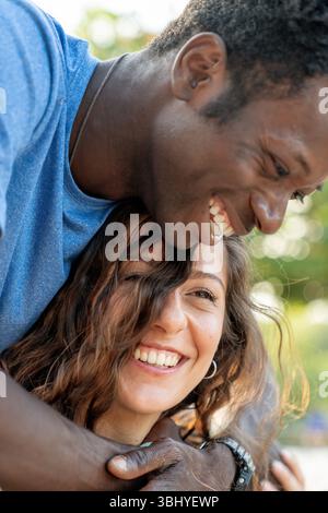 An intimate close-up portrait of a happy, diverse young couple embracing and laughing outdoors. A genuine moment of love, affection, and togetherness. Stock Photo