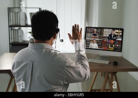 A virtual meeting and virtual conference man white shirt participating virtual meeting computer waving to screen with multiple people video call Stock Photo
