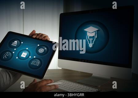 An e-learning platforms image shows person holding tablet with educational icons displayed, front of computer monitor with graduation cap Stock Photo